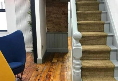 Communal area featuring a wooden floor, blue armchair, and a modern staircase with sisal carpet.