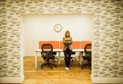 Office workspace viewed through a framed opening, featuring wood floors and orange desk dividers.
