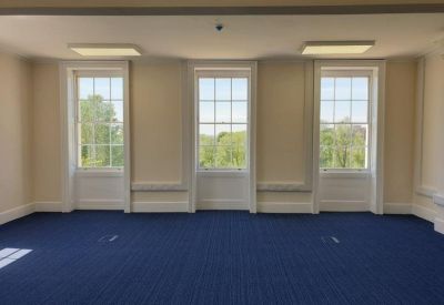 Spacious, empty room with blue carpet and three large vertical windows.