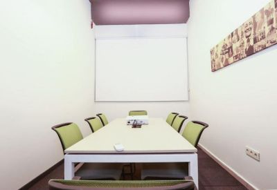 Meeting room with a white table, green chairs, and a projector screen.