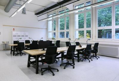 Bright open-plan office space featuring long wooden desks and ergonomic black chairs.