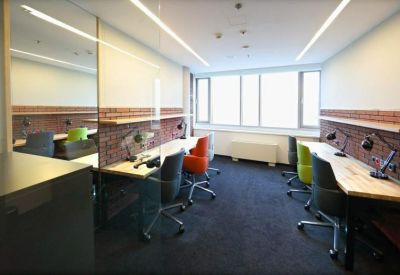 Shared office space with long white desks, colorful rolling chairs, and exposed brick details.