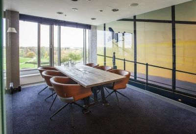 Sunlit meeting room with a rustic wooden table, tan leather chairs, and floor-to-ceiling windows.