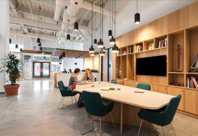 Modern meeting area with a long white table, dark teal chairs, and wooden shelving unit.