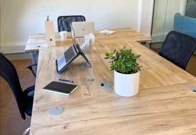 Bright office workspace with wooden desks, a potted plant, and framed nature photography.
