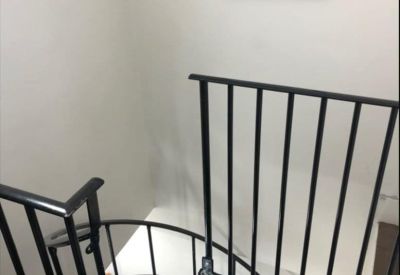 View looking down a black metal spiral staircase from a landing with framed art.