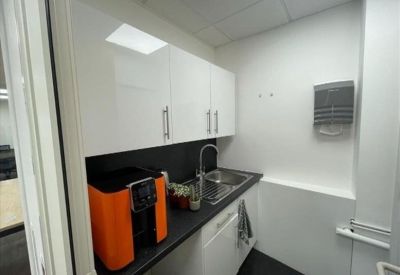 Sleek office kitchenette with white cabinetry and a modern coffee machine.
