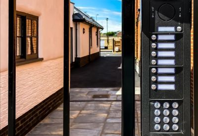 Secure building entrance featuring a black intercom system and keypad next to a brick walkway.