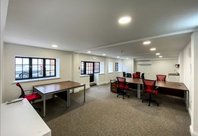Spacious open-plan office with multiple workstations, red ergonomic chairs, and grey carpeting.