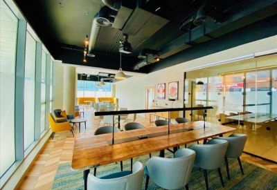 Bright open-plan office space with long wooden hot-desking tables and industrial ceilings.