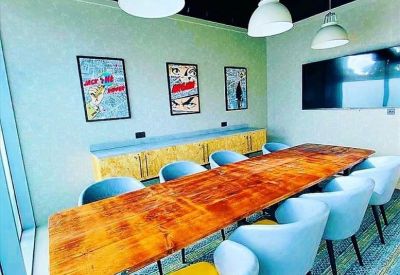 Modern meeting room with a long wooden table, light blue chairs, and pop-art wall decor.
