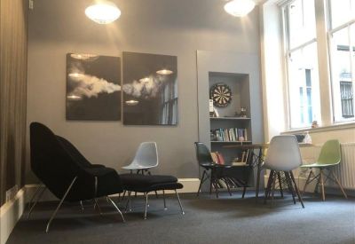 Lounge area with comfortable armchairs, a dartboard, and large windows.