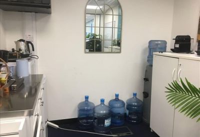 Communal kitchen area with water jugs, a coffee machine, and an arched wall mirror.
