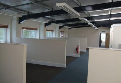 Open-plan office with white partition walls, dark carpets, and industrial black ceiling beams.