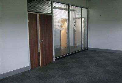 Hallway featuring a dark wood door and glass partitioning leading to bright office rooms.