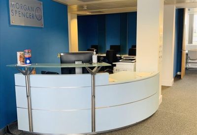 Curved white reception desk with glass countertop in front of a blue wall with company branding.