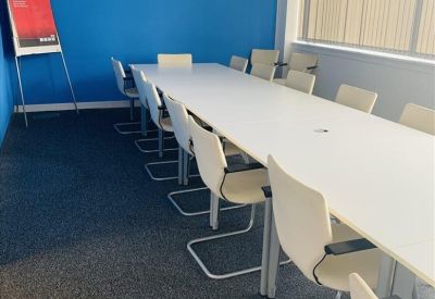 Long white boardroom table with cream-colored chairs and a vibrant blue feature wall.