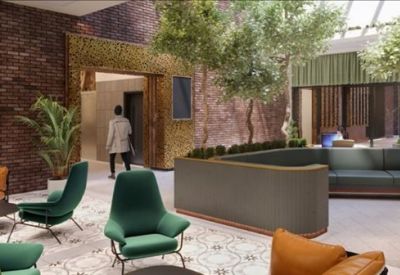 Bright indoor lounge area with velvet green armchairs, trees, and a brick feature wall.