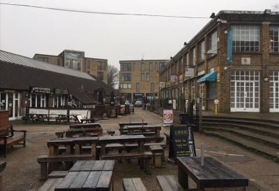 Outdoor communal area with wooden picnic tables in a courtyard between brick buildings.