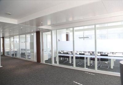 Glass-walled corridor looking into a professional boardroom with rows of black chairs.