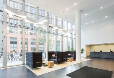 Bright, high-ceilinged building lobby with double-height windows and minimalist black lounge seating.