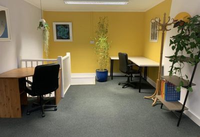 Bright workspace featuring a yellow accent wall, two desks, and indoor plants.
