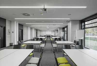 Symmetrical view of a large seminar room with white tables and green-accented chairs.