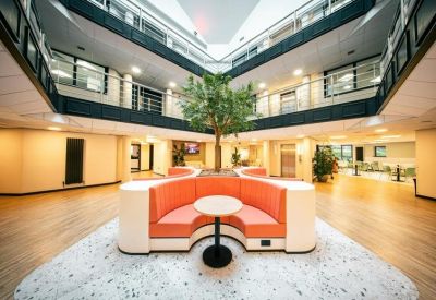 Impressive multi-story atrium with a central tree, curved orange seating, and glass balconies.