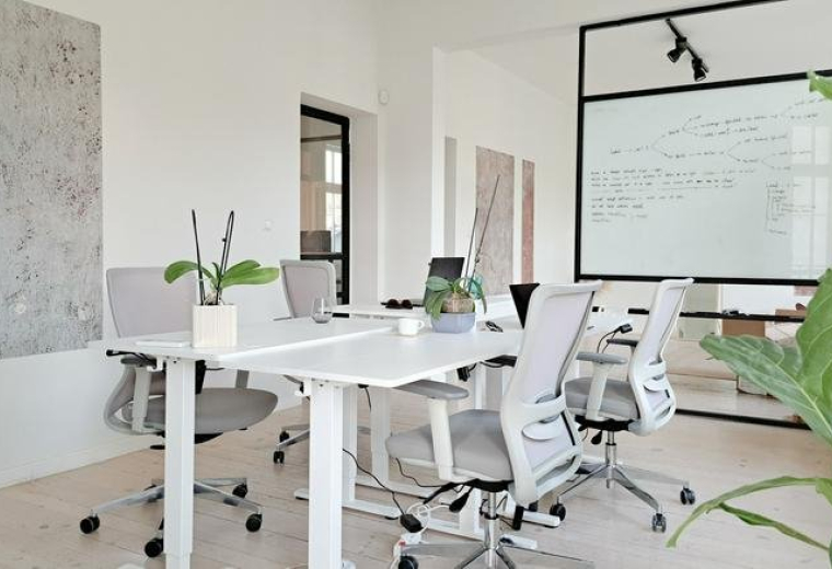 Meeting room with white desks, ergonomic chairs, and a whiteboard.