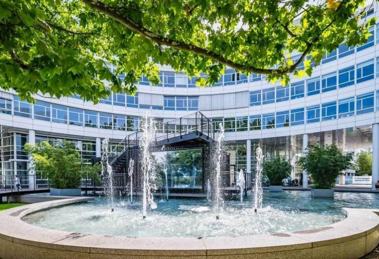 Exterior view of the curved glass-facade building at St. -Martin-Straße with a central courtyard fountain.