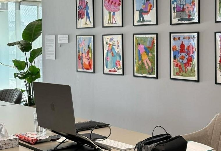 Open-plan office with art on the walls and a laptop on a desk.