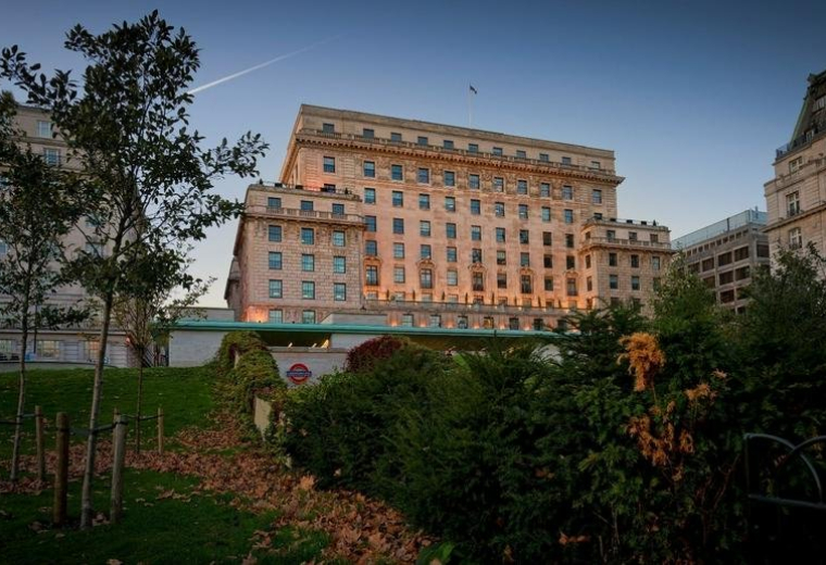 Grand stone exterior of Devonshire House viewed from a park at dusk.