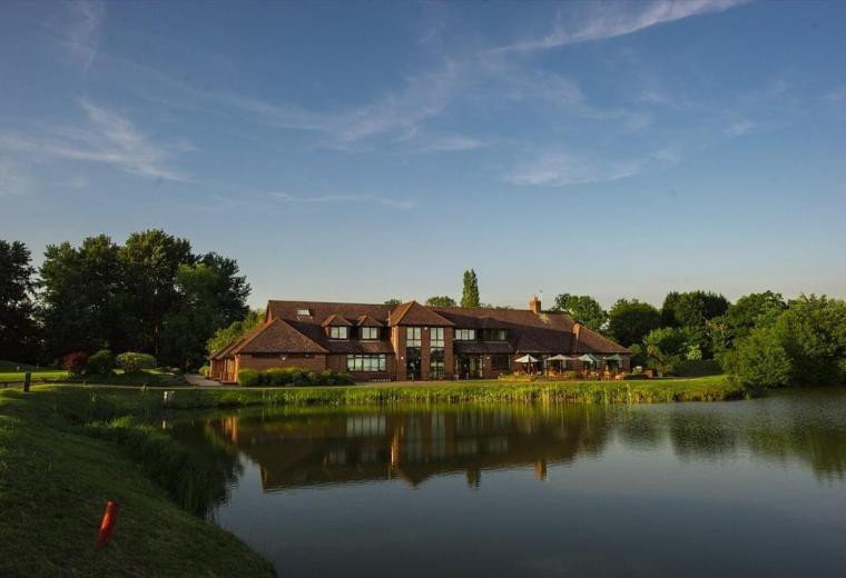 Exterior view of the brick building at Pyrford Golf Club reflecting in the adjacent lake.