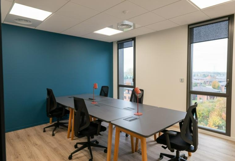 Modern office workspace with dark grey desks and tall windows providing natural light.
