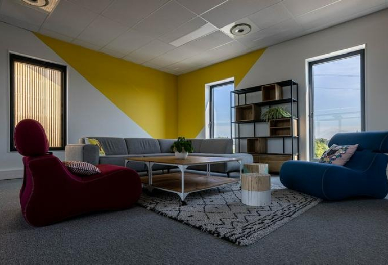 Spacious communal lounge at COLOFT Arteparc Lesquin with colorful seating and a yellow geometric wall mural.