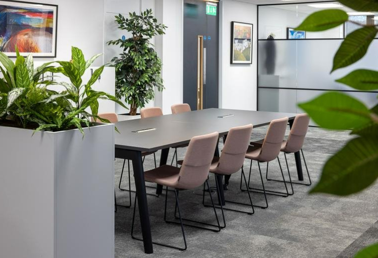 Modern conference room with a long dark table, pink upholstered chairs, and greenery.