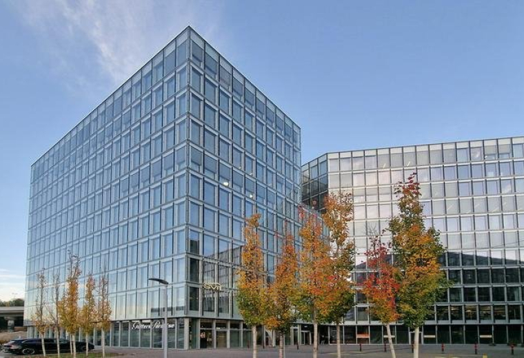 Exterior view of a large modern glass office complex with autumn trees.