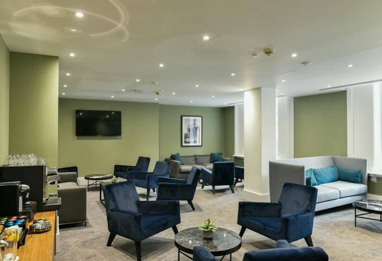 Lounge area featuring velvet blue armchairs, a television, and a coffee station.