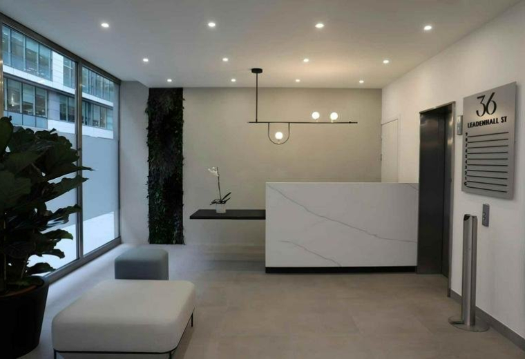 Minimalist white reception desk with a contemporary pendant light and green wall feature.
