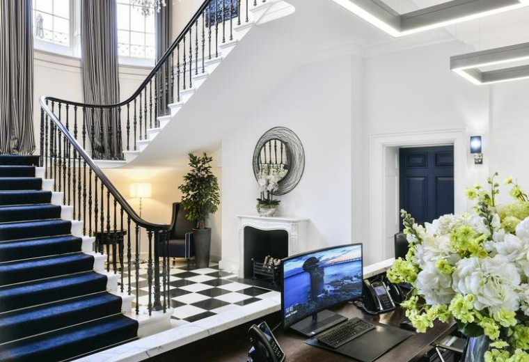 Bright reception area with a grand staircase, blue carpet, and checkered flooring.