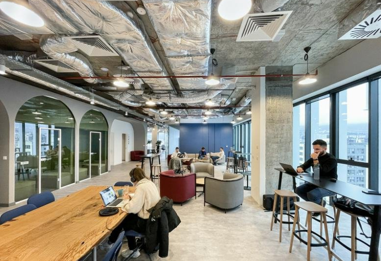 Lively coworking lounge at Advance Business Center with industrial ceilings and natural wood tables.