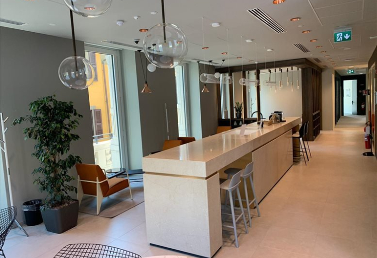 Bright shared office space with white desks, black chairs, and large windows.