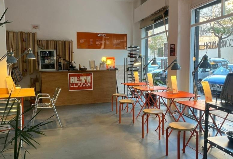 Bright open-plan coworking space with orange cafe tables, wooden stools, and a reception desk.