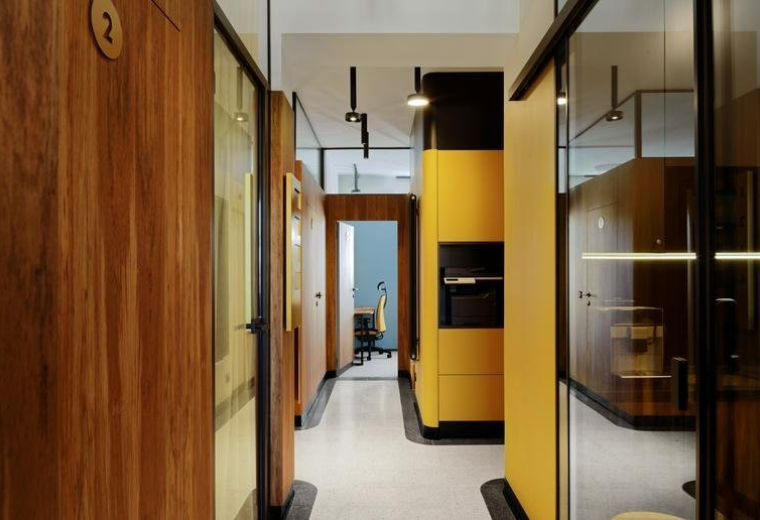 Hallway at 152 Puławska with warm wood paneling, glass partitions, and vibrant yellow cabinetry.