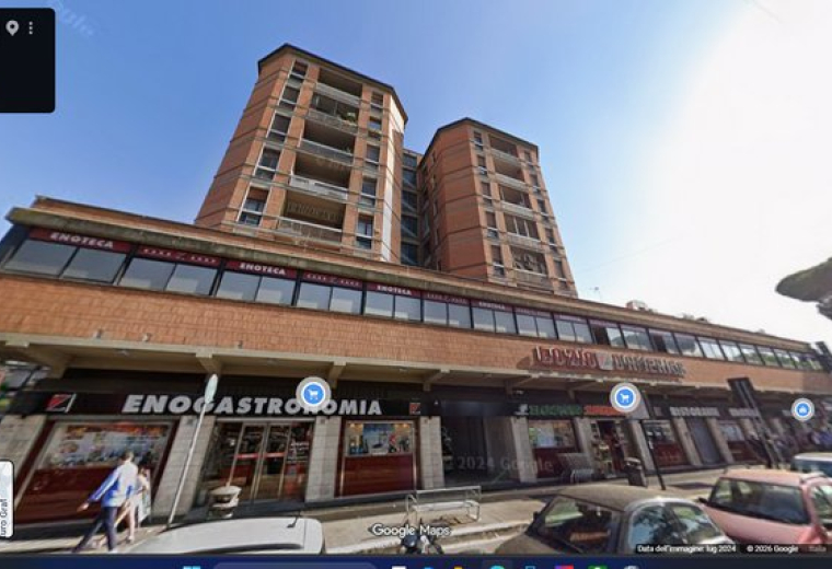 Street-level view of the brick mixed-use building at 16, Via Ugo Ojetti with retail shops and residential balconies.