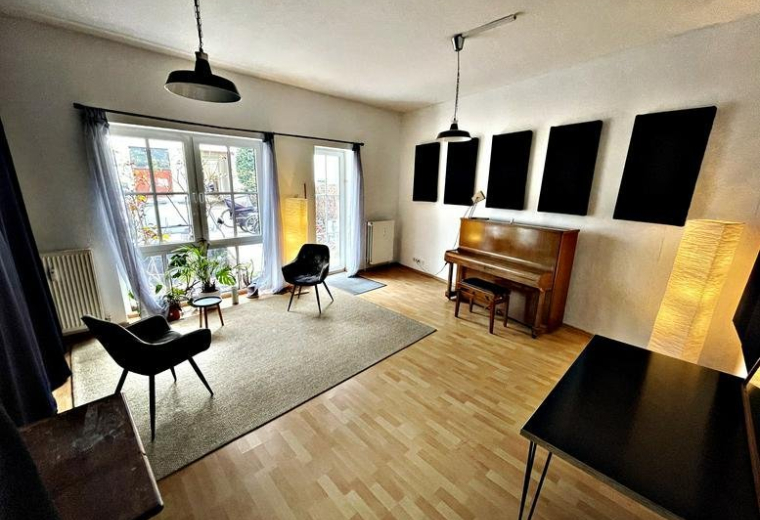 Bright multi-purpose room featuring soundproofing panels, a piano, and lounge seating.