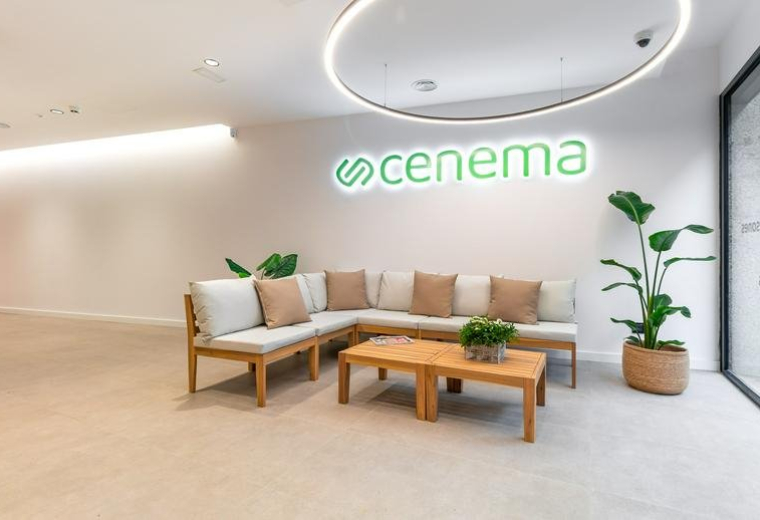 Reception area at 261, Carrer de Sardenya with a wooden L-shaped sofa, green plants, and branded signage.