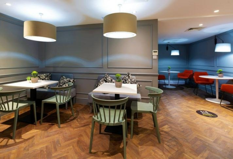 Spacious dining and breakout area with green chairs and wooden herringbone floors.