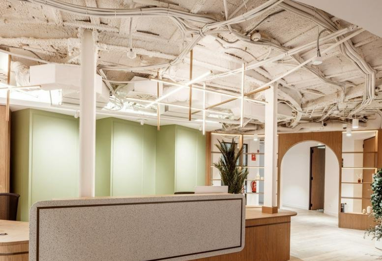 Modern reception desk at 56, Passeig de Gràcia, with a textured front and industrial ceiling.