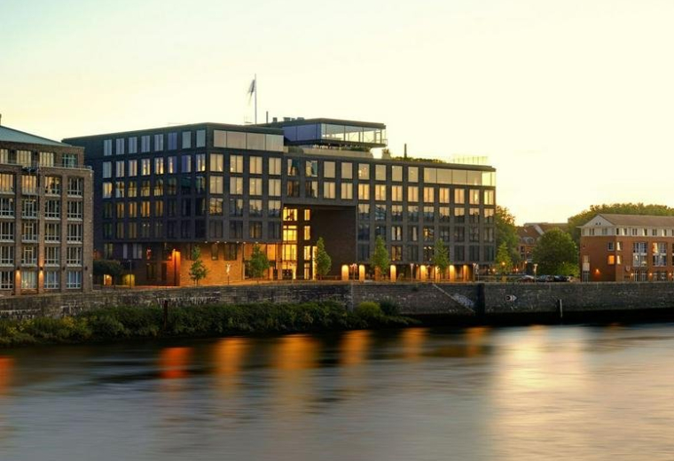 Exterior view of the dark-brick building 59, Teerhof at dusk with river reflections.